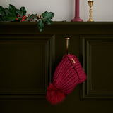 Barbour SALTBURN Womens Beanie Biking Red hanging on a hook with faux fur pom pom, showcasing the textured knit design.