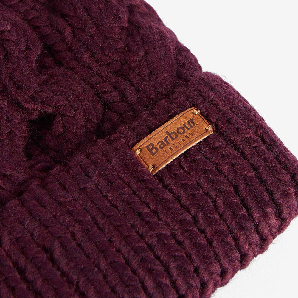 Barbour PENSHAW Womens Pom-Pom Beanie Bordeaux detailed view showing cable-knit structure and logo-embossed leather badge.