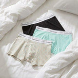 Calvin Klein COTTON BLEND Mens 3 Pack Trunks Multicoloured displayed on a bed, showing black, mint, and patterned trunks.