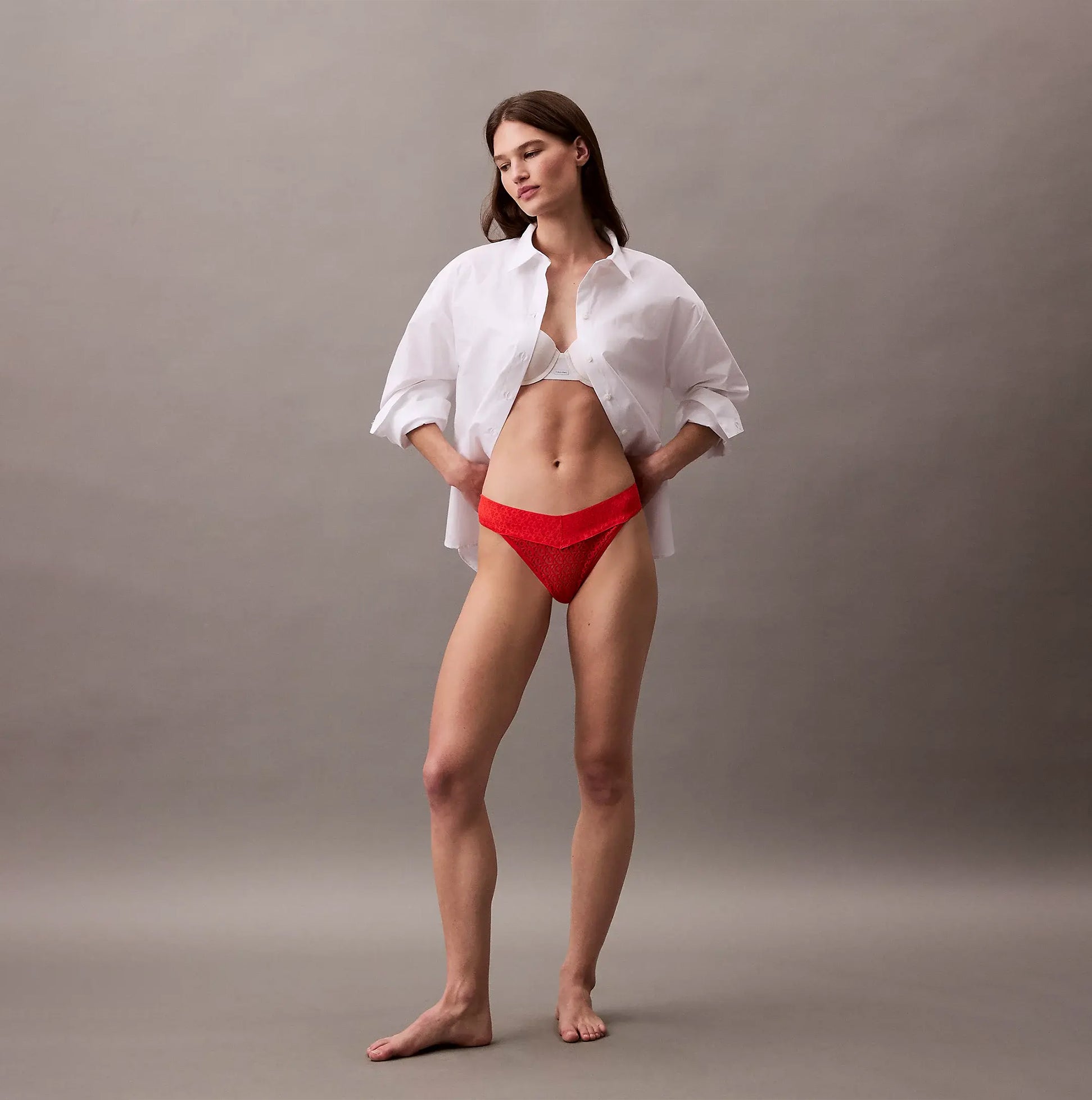 Calvin Klein THONG Womens Icon Logo Lace Molten Red worn by a model in a side view with a white shirt, showcasing the lace detail.