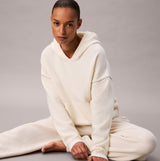 Calvin Klein PLUSH HOODIE. Womens Ivory. Front view on model seated, showcasing soft fabric and relaxed fit.