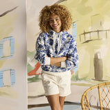 Joules MILBOURNE Womens Hoodie Blue Safari front view model smiling against a colorful backdrop.