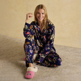 Joules ALMA Womens Pyjama Set Navy Floral model sitting smiling in floral navy pyjama set with pink slippers