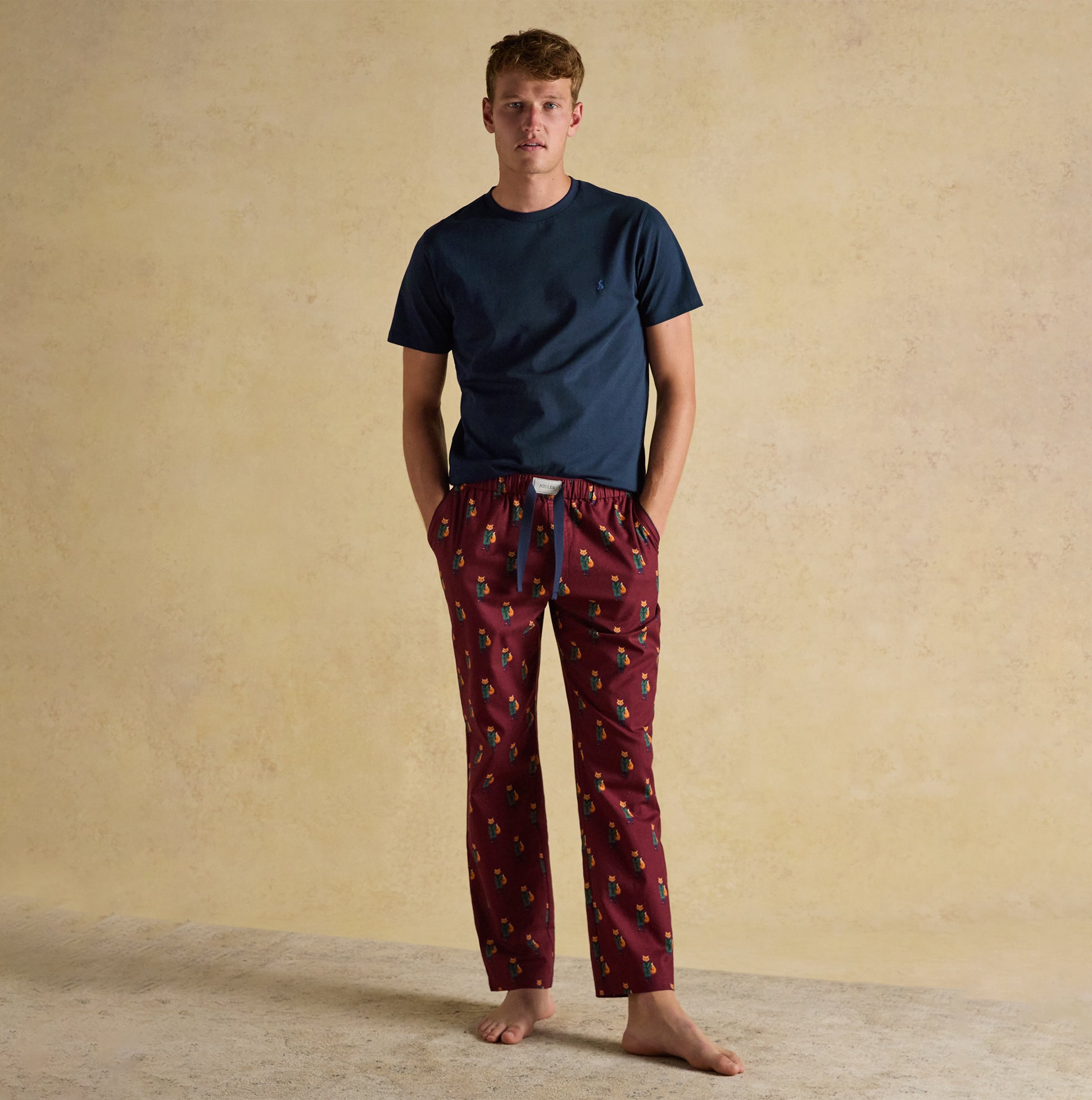 Joules DOZER Mens Pyjama Trousers Burgundy Red front view worn with a blue t-shirt, showcasing relaxed fit and intricate pattern.