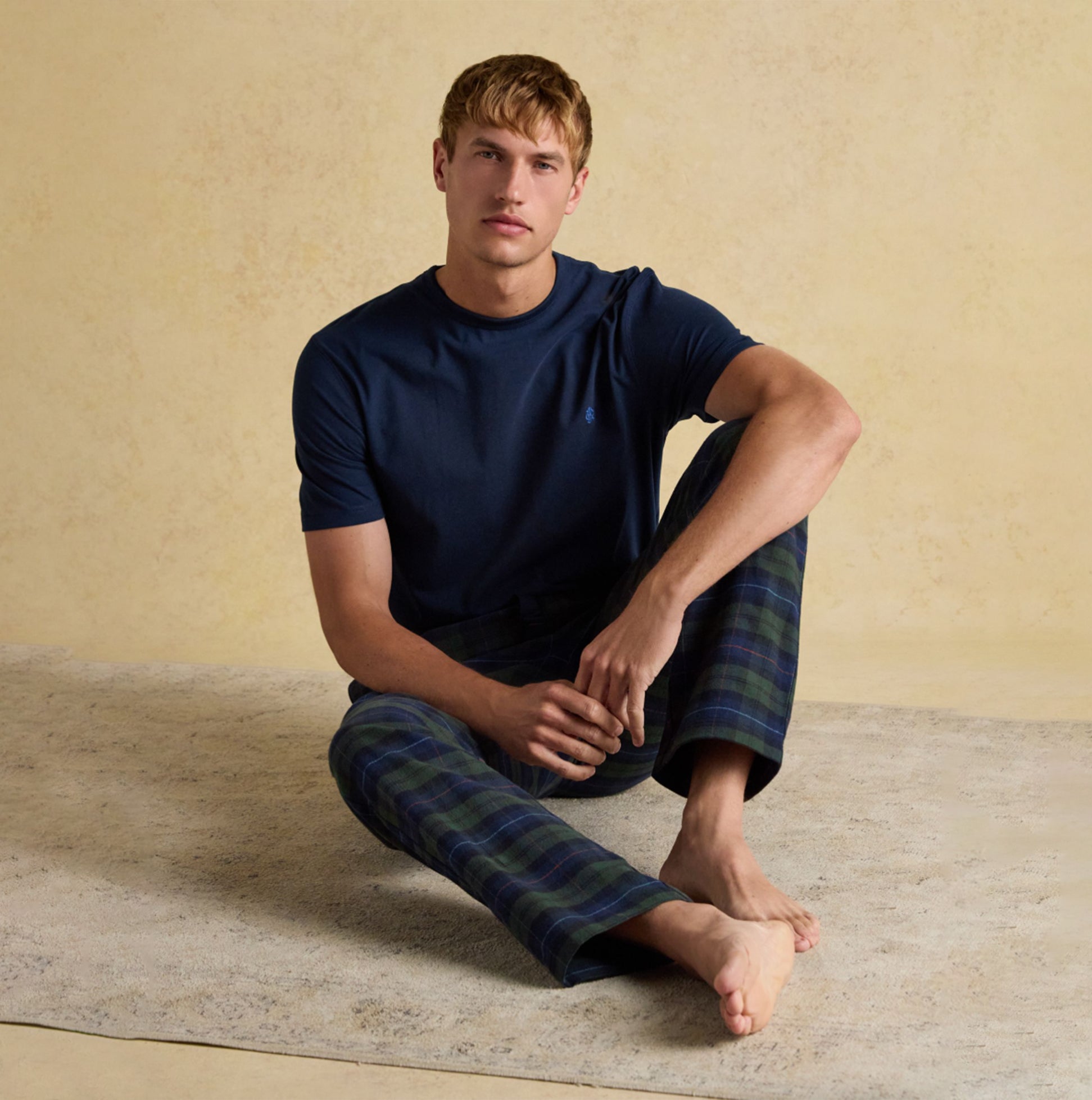 Joules DOZER Mens Pyjama Bottoms Green/Navy side view of model sitting in relaxed fit cotton pants with navy t-shirt.