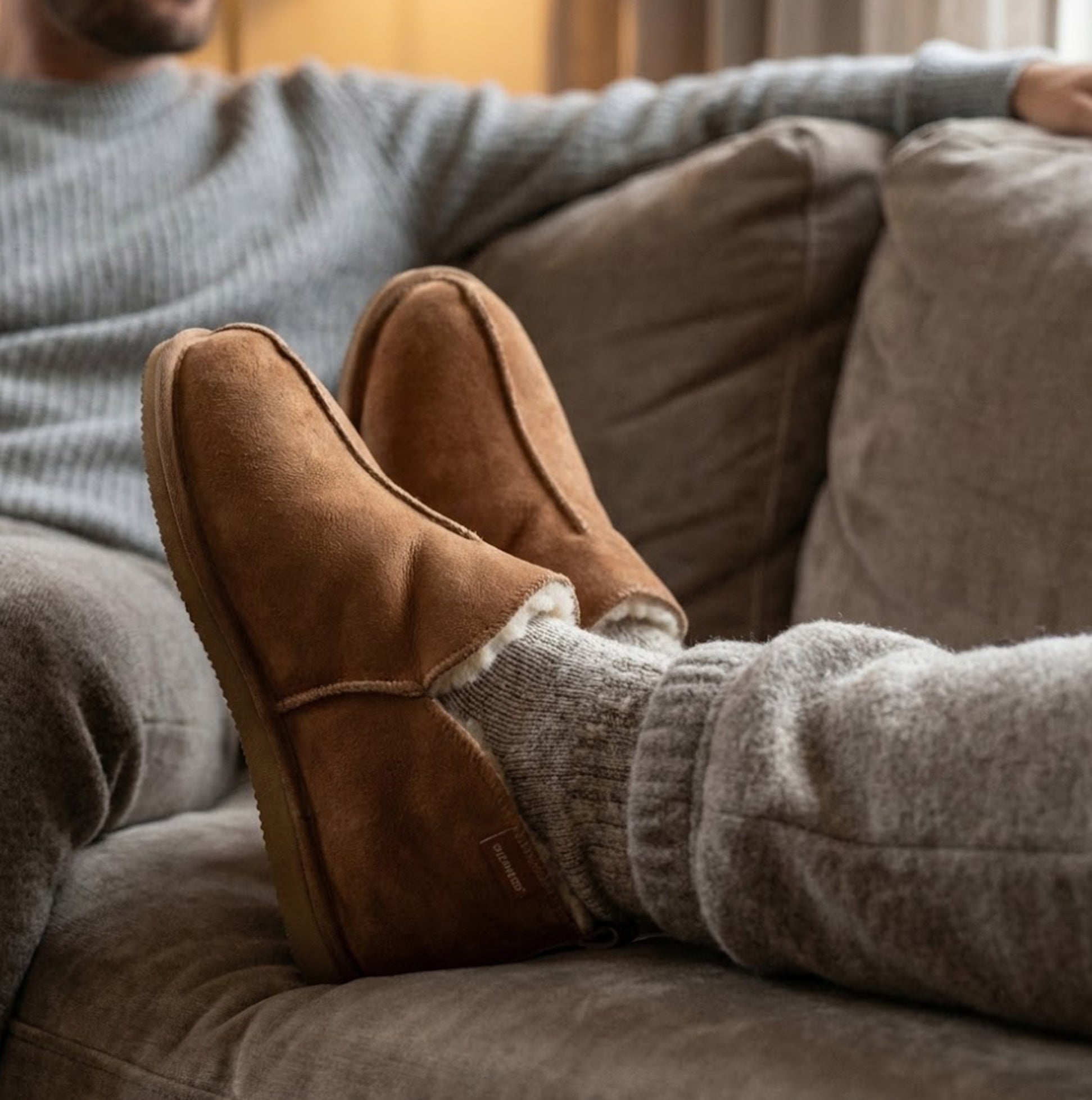 Shepherd ANTON Mens Sheepskin Slipper Boots Brown side view on feet while sitting on a couch, showcasing comfort and style.