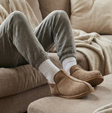 Shepherd ANNIE Womens Sheepskin Slipper Boots Stone side view being worn with gray joggers on a couch.