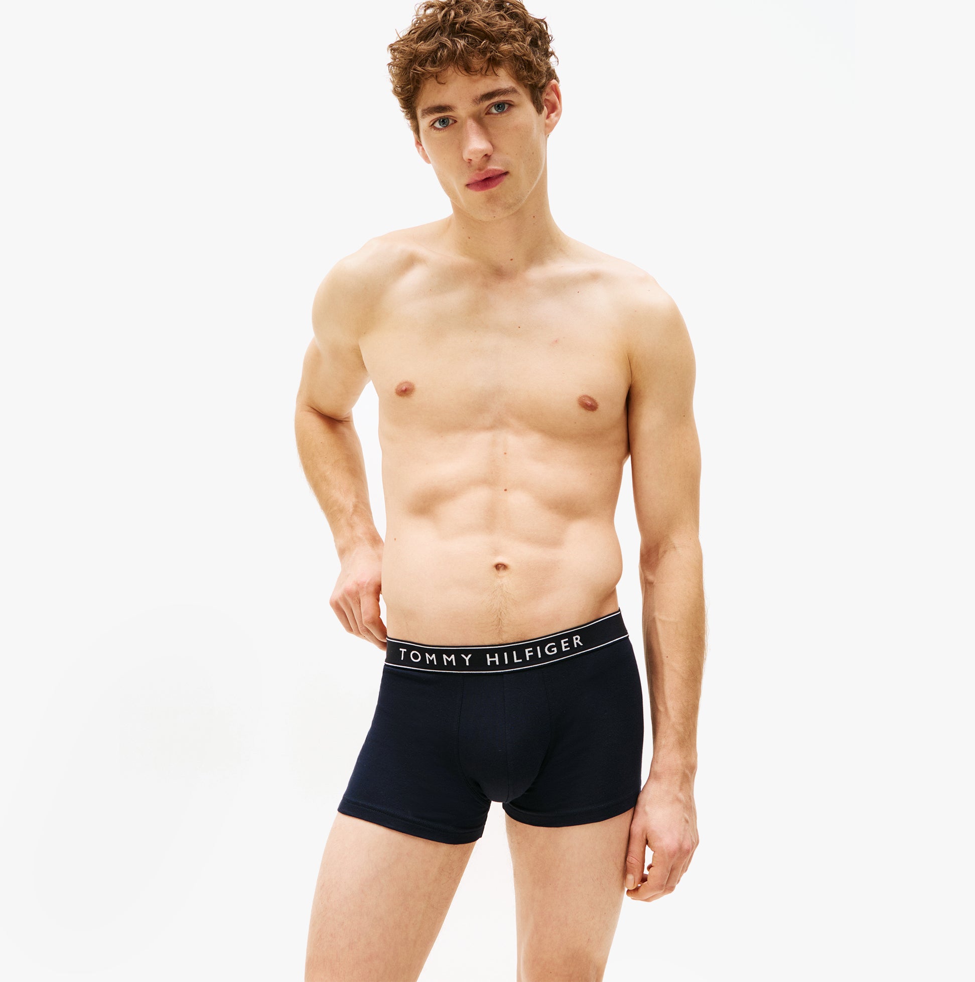 Tommy Hilfiger 3 Pack Mens Trunks Des Sky/Calico/Fssl Blue front view featuring model wearing navy trunks with logo waistband.