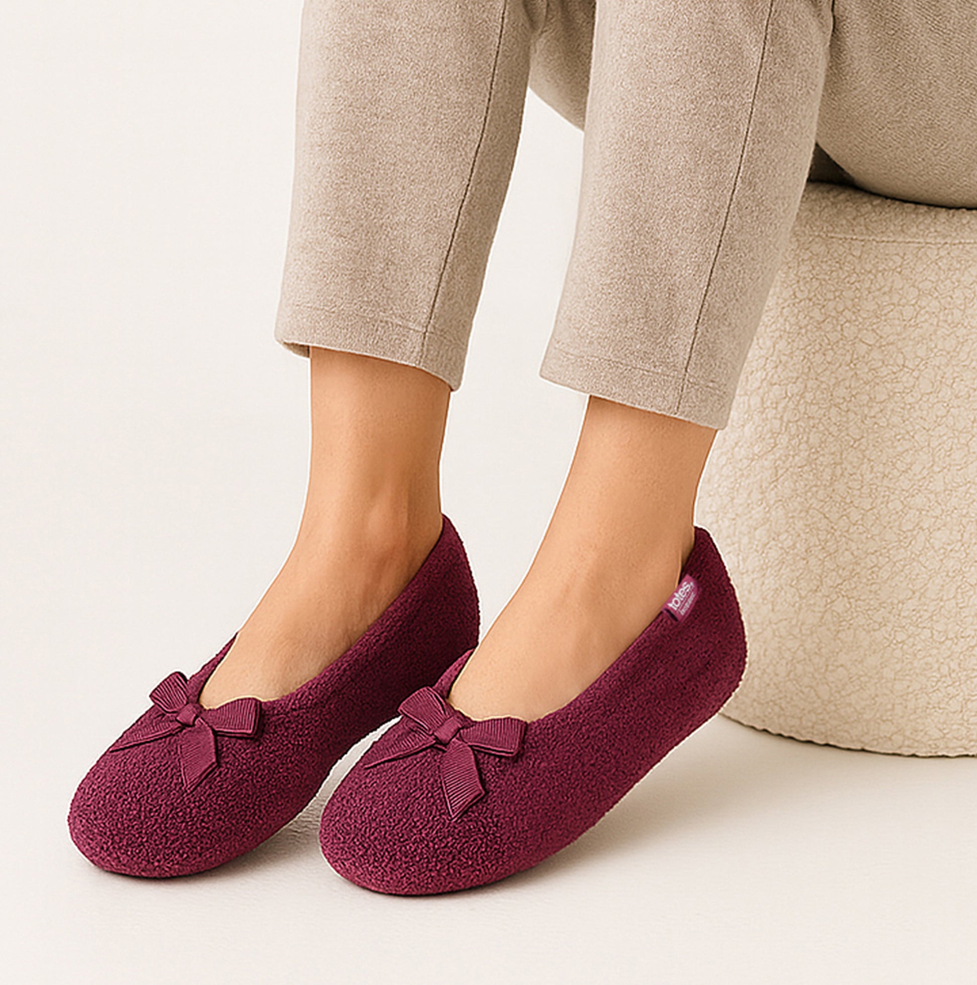 Totes Isotoner STRETCH TERRY BOW Womens Ballerina Slippers Burgundy side view on a model's feet, featuring a bow detail.