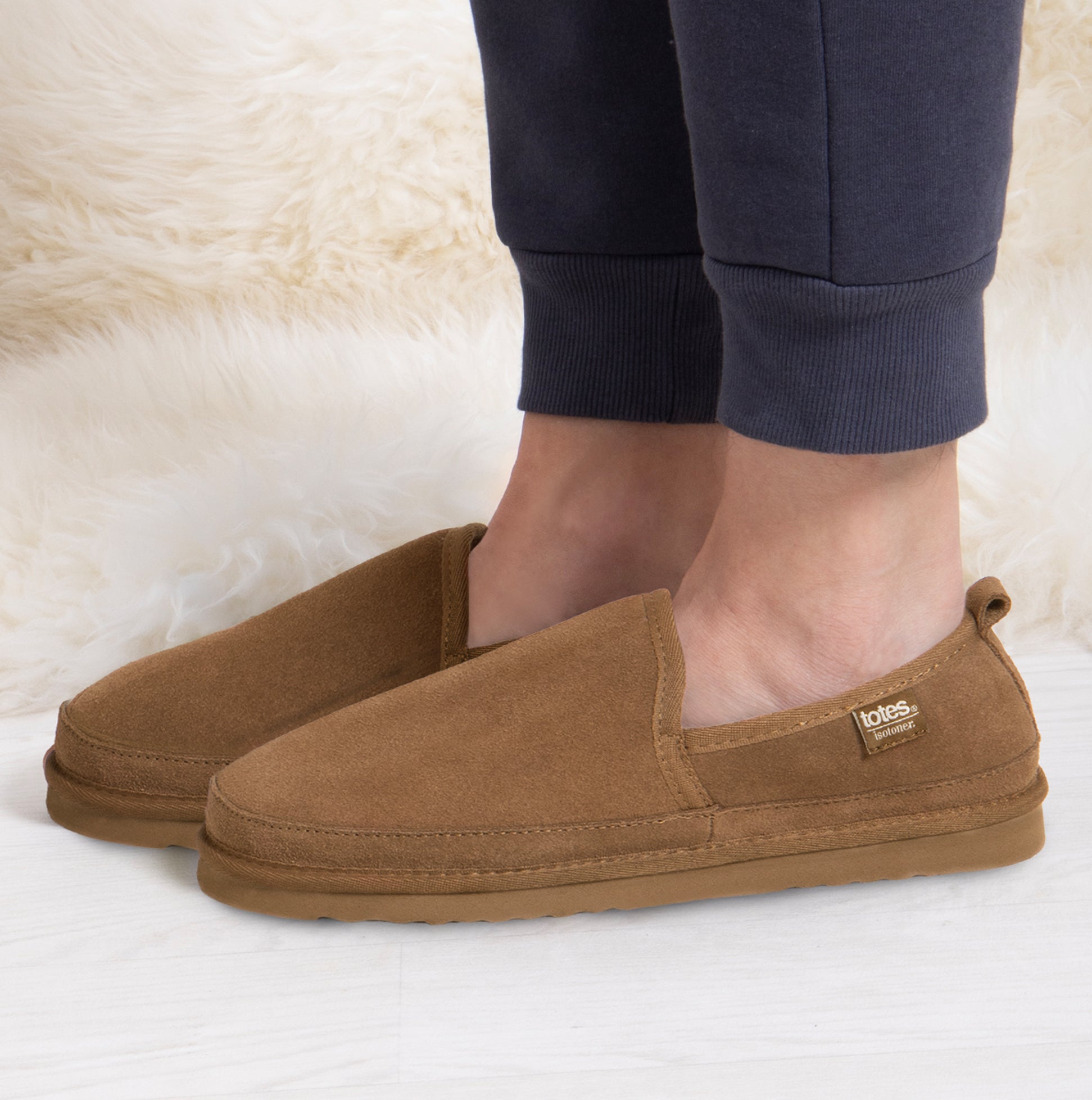 Totes Isotoner REAL SUEDE FULL BACK Mens Full Back Slippers Tan side view worn by a person in casual attire.
