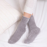 Totes Toasties FAIR ISLE Chenille Womens Socks Grey side view on feet, contrasting with white bedding.